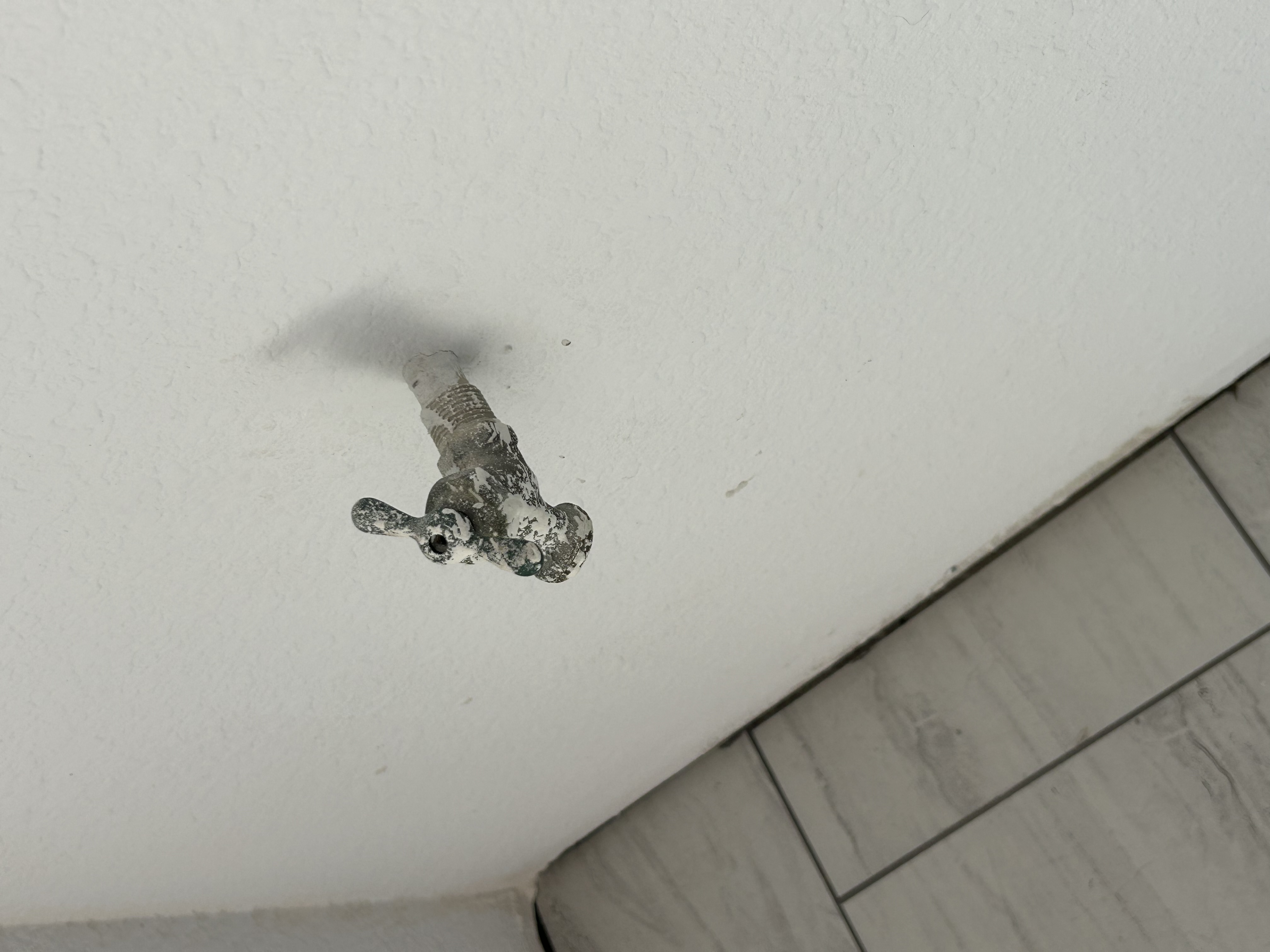 Old corroded hose bib protruding from interior wall inside water heater cabinet