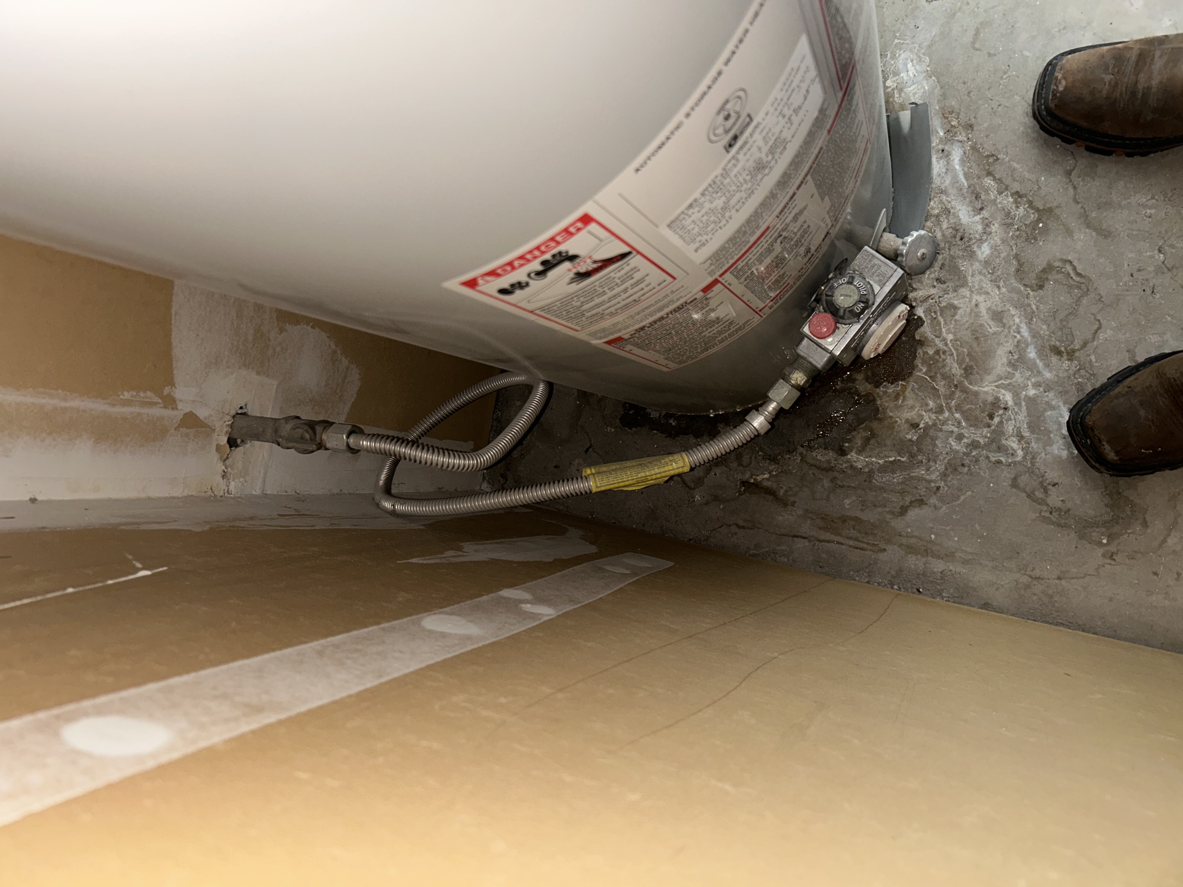 Old gas water heater gas connections at base with water on floor from ongoing leak