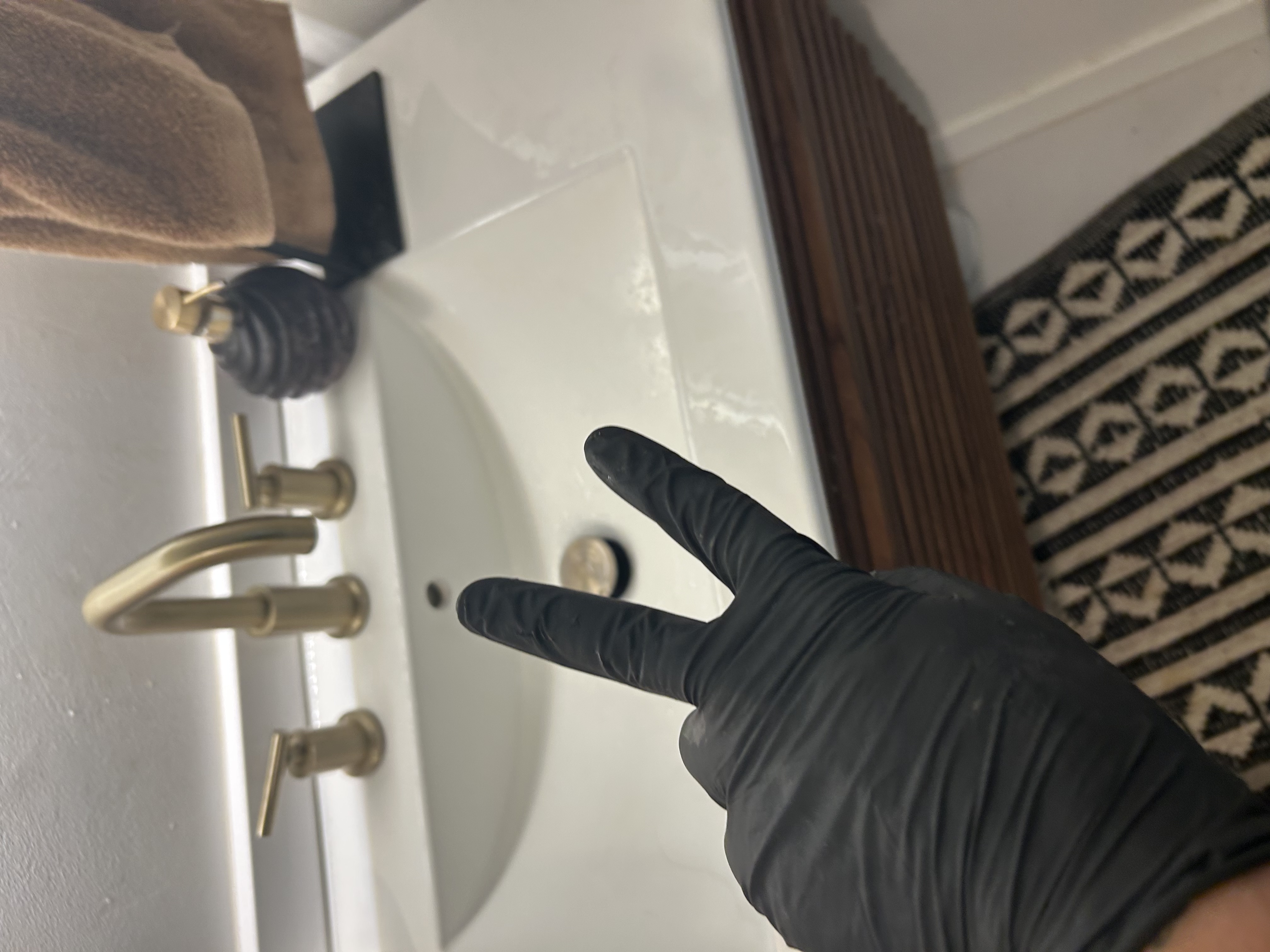 Guest bath sink in Scottsdale AZ rental property — white porcelain with gold fixtures, gloved hand at slow drain before service — Desert Rain Plumbing