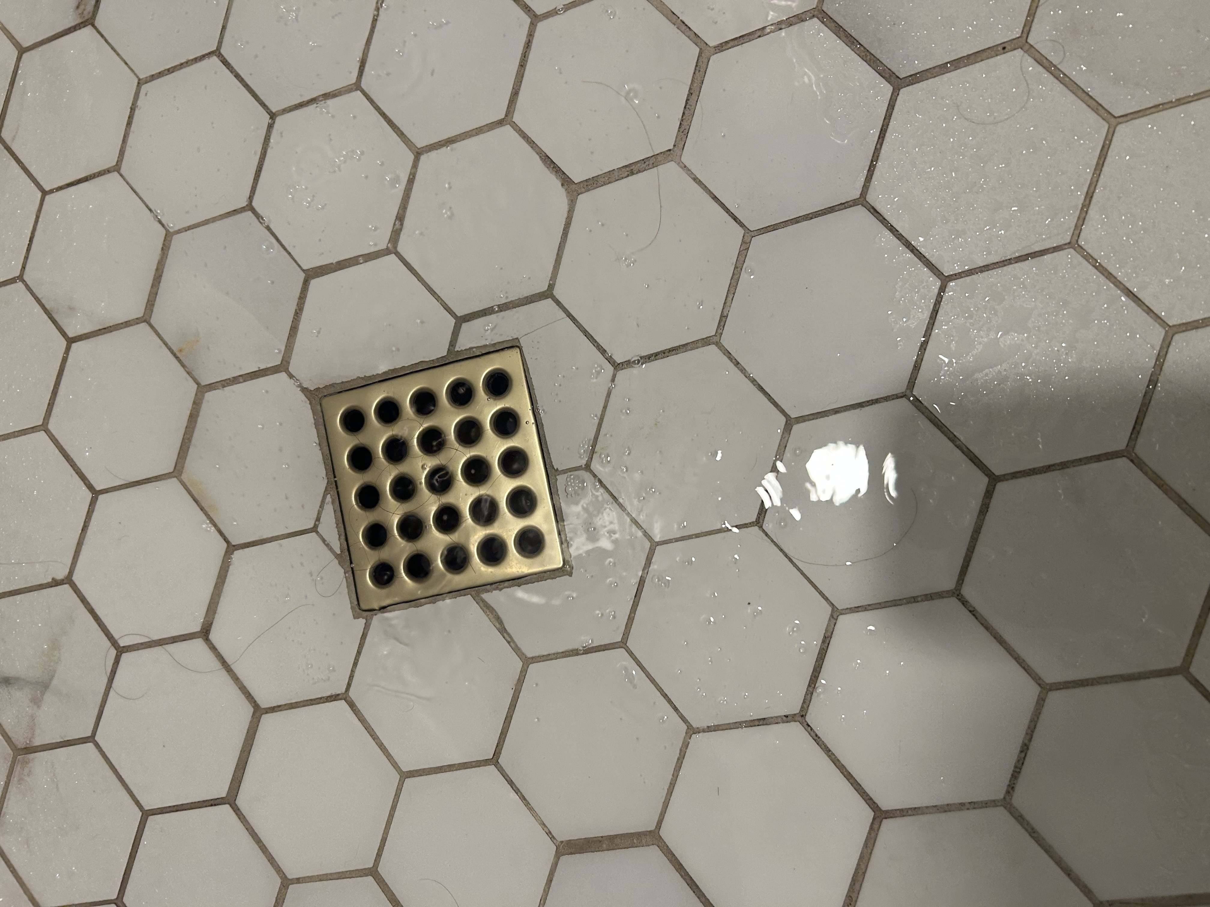 Close-up of brushed-gold square shower drain cover on hexagonal tile floor — Scottsdale AZ — Desert Rain Plumbing